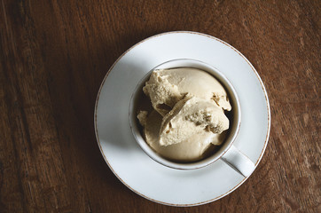 White coffee cup filled with soft coffee flavoured ice cream on dark wooden background. View from above.