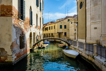 An old canal in Venice with parked boats and a small pedestrian bridge