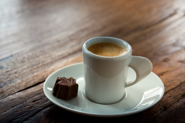 A cup of espresso with a chocolate candy maple leaf shaped on wooden background