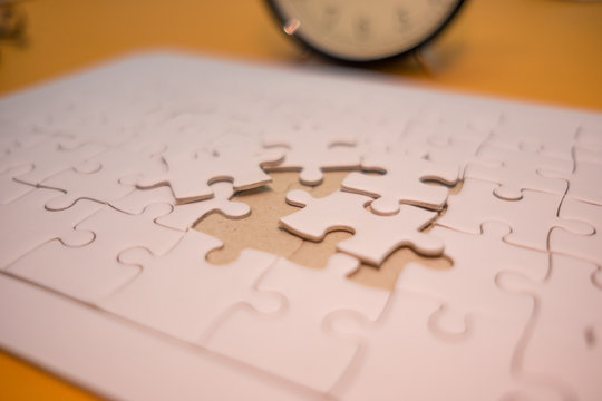 business background white jigsaw placed on orange table with clock and copy space. image for texture, problem, thinking, idea, toy, time, success, game concept