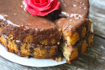 Handmade sponge cake with chocolate frosting. Small cake with cacao ganache glaze. Red sugar rose decorated. Homt pastry. Sweet dessert. Cute birthday cake present.