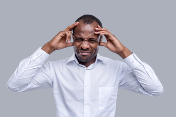 Terrible headache. Attractive unhappy dark-eyed afro-american man wearing a white shirt and touching his temples and having a terrible headache