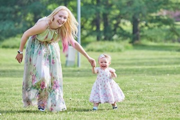 Mother and her little daughter playing in the garden, hugging and kissing on a sunny summer day