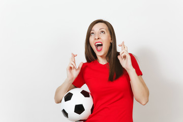 European young woman football fan or player in red uniform keep fingers crossed hold soccer ball isolated on white background. Sport play football lifestyle concept. Wait for special moment. Make wish