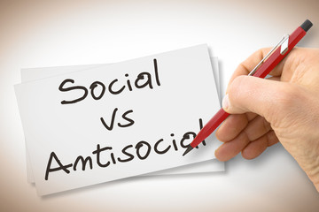 Hand writing Social Vs Antisocial with a pencil on a blank sheet - concept image