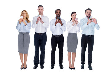 Obraz premium Addiction. Good-looking young unsmiling addicted colleagues standing in one line and using their phones and having stony-faced expression