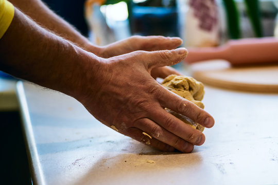 Skillful man's hands roll out dough on the white table