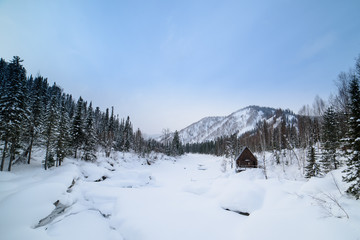 Fototapeta na wymiar Winter, a house in the mountains on the bank of a frozen river.