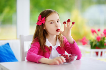 Pretty little girl eating raspberries at home. Cute child enjoying her healthy organic fruits and berries.