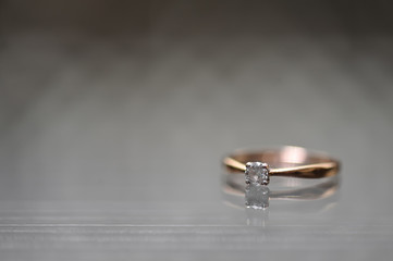 A beautiful engagement ring lies on the glass surface and is reflected. Macro photography