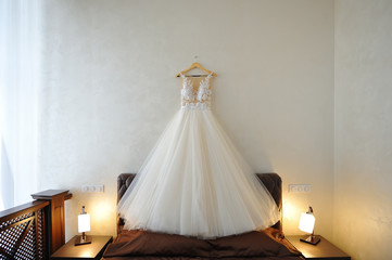 Wedding dress of the bride hangs over the bed in a beautiful room