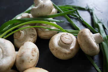 Raw champignons with green onion on black background top view