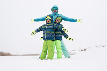 Fototapeta na wymiar A happy mother with kids in sunglasses and a bright blue ski suit. Mother and children are happy together. A sports family on a snow-covered river with snow. Boys are very happy to play outdoors