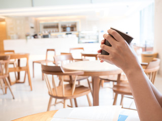 woman hand hold hot coffee cup in emply cafe