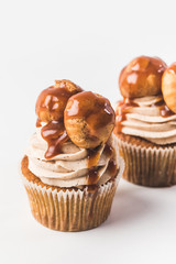 close up view of cupcakes with cream, profiteroles and caramel isolated on white