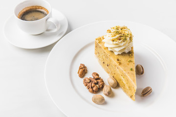 close up view of piece of cake with nuts and cup of coffee isolated on white