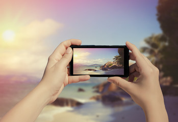 Female hand taking picture of La Digue island on mobile phone. Picture of Seychelles island on smart phone