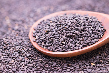 Black sesame in wooden spoon on sesame background.