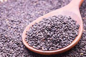 Black sesame in wooden spoon on sesame background.