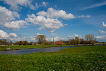 typische Landschaft der Wesermarsch mit grüner Weide, einem Siel und lebhaftem blauen Himmel mit...