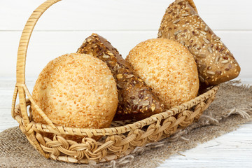 Bread buns in wooden basket on white wooden background