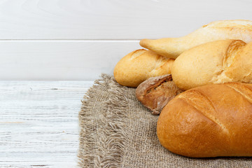 Plenty bread background. Bakery and grocery concept. Fresh, healthy rye and white loaves, sprinkled flour on sackcloth and rustic wood table, food closeup