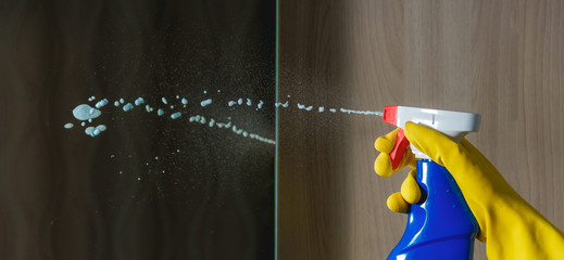 Female Hand in Yellow Glove Cleaning Mirror with Spray Cleaner. in Blue Bottle, Housework, Spring Cleaning Concept.