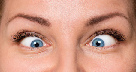 Close-up scared face of beautiful young woman with beautiful blue eyes and big pretty eyelashes and eyebrows. Macro of human eyes - surprise or shock, looking away.