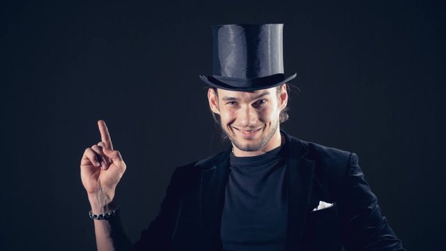 A man in a top hat and a suit is lifting his head and his index finger