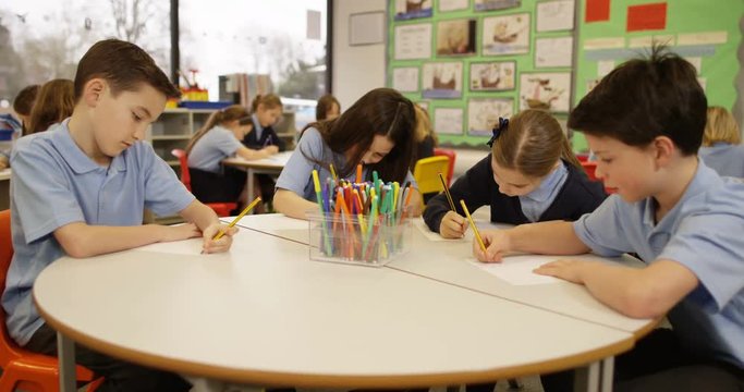 4K Young school children working in groups in class, colored pens on the desk & children's artwork on the wall behind. Slow motion