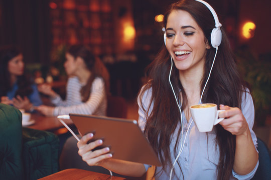 Young woman listening to music via digital tablet and headphones and drink coffee in a cafe - Powered by Adobe
