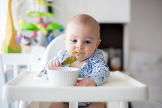 Cute little baby boy, eating mashed vegetables for lunch, mom feeding him