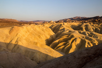 Fototapeta na wymiar Setting sun on the eroded mountain ridges of desert dry and hot landscape at Zabriskie Point Death Valley National Park, California, evening time of sunny day before sunset