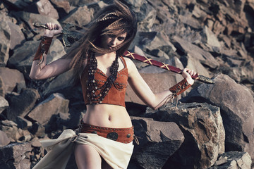 Beautiful girl in the clothes of a Viking or Amazon, with a sword on a background of stones.