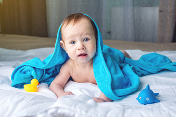 Happy baby with blue eyes lying on a blanket with a duck wrapped in a towel after bathing