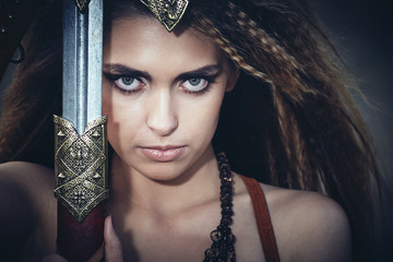 Beautiful girl in the clothes of a Viking or Amazon, with a sword on a background of stones.