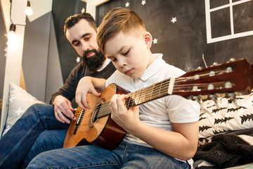 Boy showing to his father how he playing the guitar