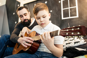Bearded man with son playing the guitar at home