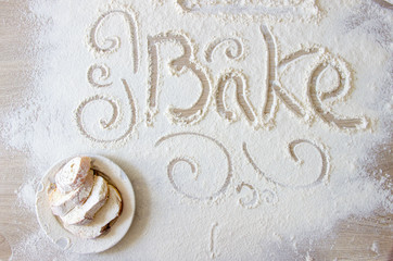 Word bake written in flour. Hand-drawn decorative elements. Plate with bread slices covered with white flour