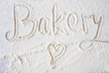 The word Bakery hand written in flour on a wood table. Hand drawn heart