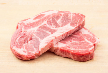 Raw pork neck meat cuts isolated on wood background fresh two slices without bone .