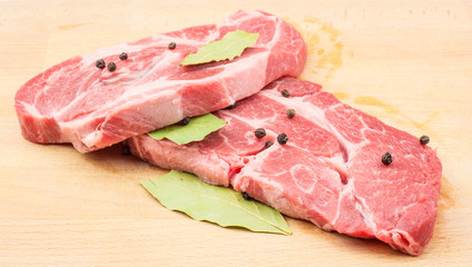 Raw pork neck meat cuts with black pepper and bay leaves on wood background fresh two slices without bone .