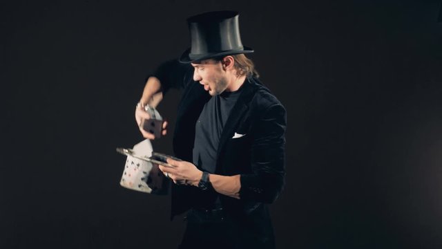 A male wizard is playing tricks with cards and transforming them into a hat