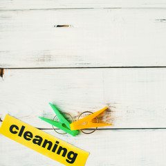 Cleaning inscription and colorful clothes pegs on a white wooden background