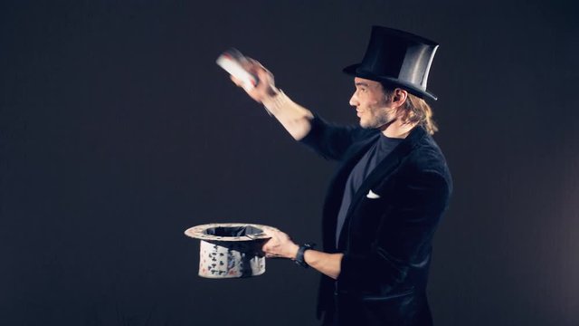 A male illusionist is performing magic tricks with cards and putting them together into a card top hat