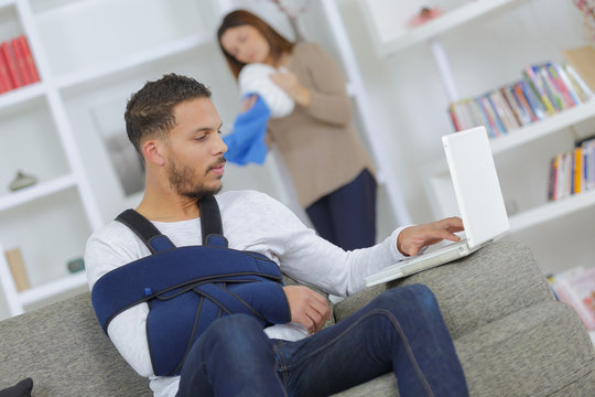 man with arm in sling using computer woman dusting