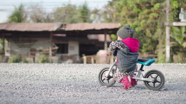 Asian boy about 1 year and 11 months with winter jacket is riding baby balance bike on construction road at rural countryside