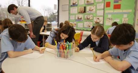 4K Young school children working in groups in classroom with teacher helping out in background. Slow motion - Powered by Adobe