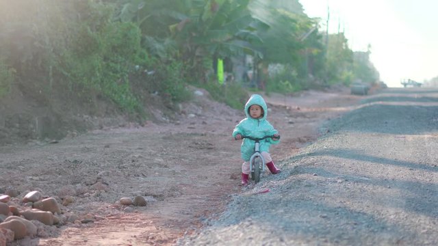 Asian boy about 1 year and 11 months with winter jacket is riding baby balance bike on construction road at rural countryside