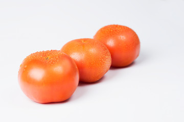 Red tomatoes on a white background with drops of water.